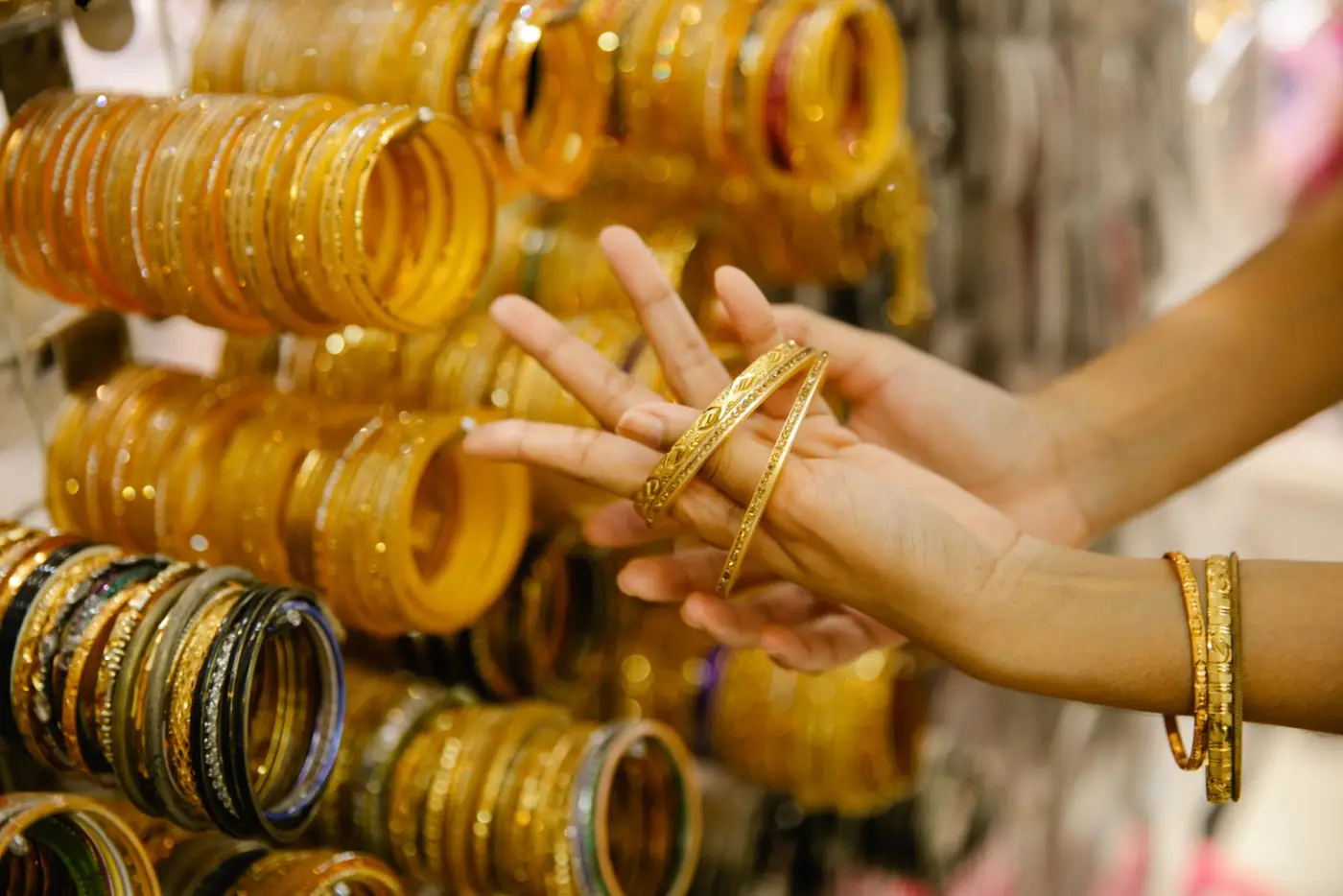 A customer's hands trying on gold bangles at a shop counter