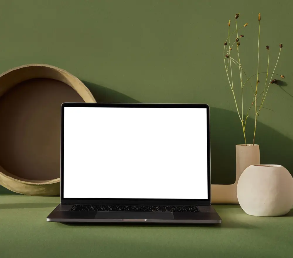 A laptop with a blank screen on a desk, against a plain green wall