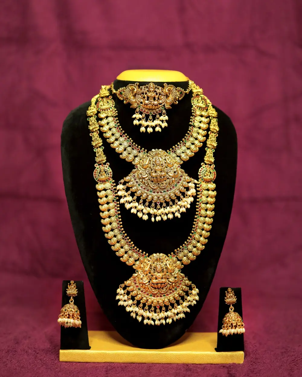 A gold bridal necklace set with matching earrings on a velvet stand
