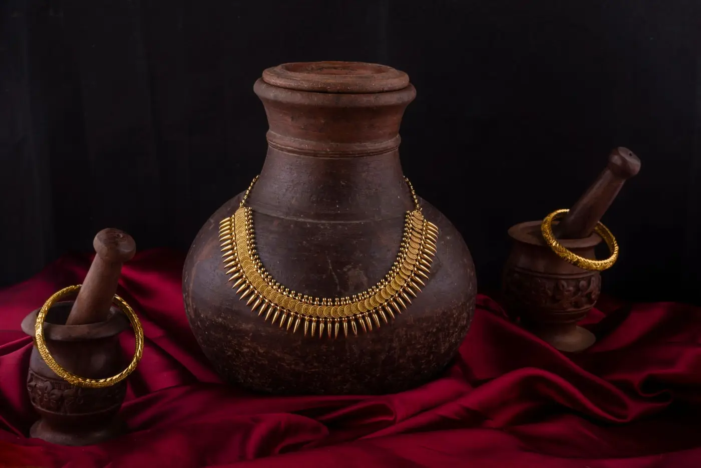 A traditional gold necklace and bangles set out on an old clay pot