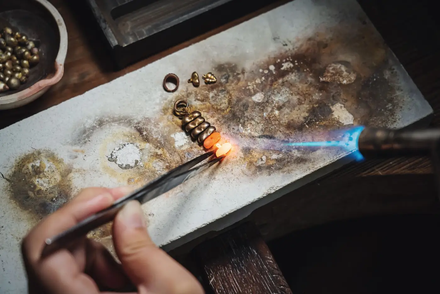 A goldsmith's torch melting a small piece of gold on a soldering block