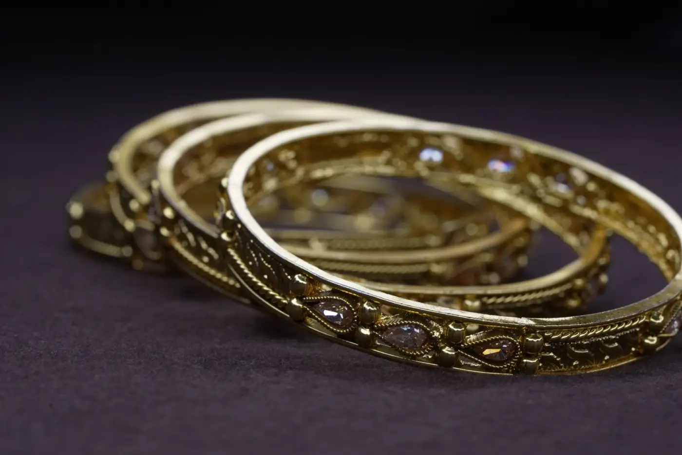 Three engraved gold bangles on a dark cloth