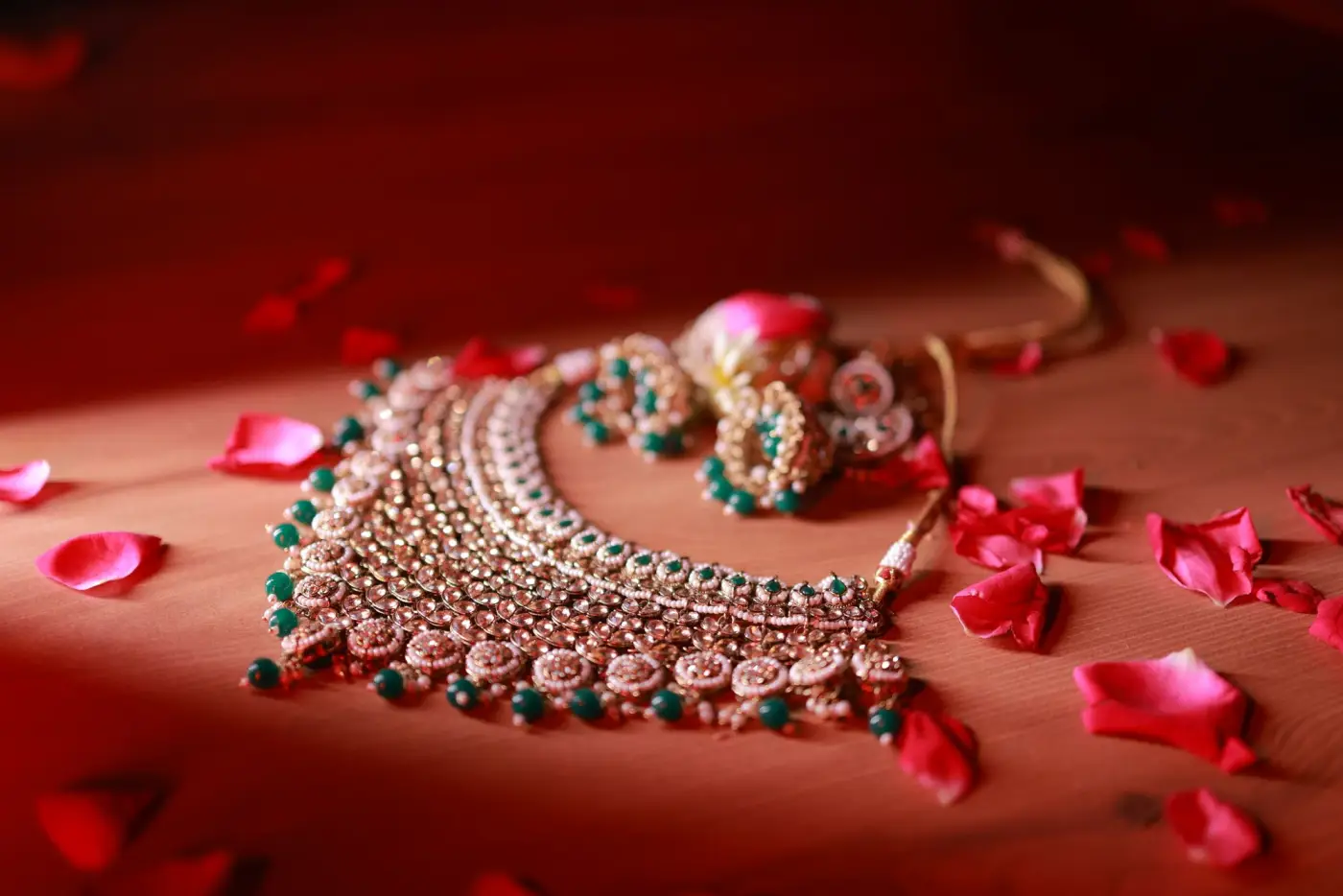 A gold bridal necklace with green stones among red rose petals