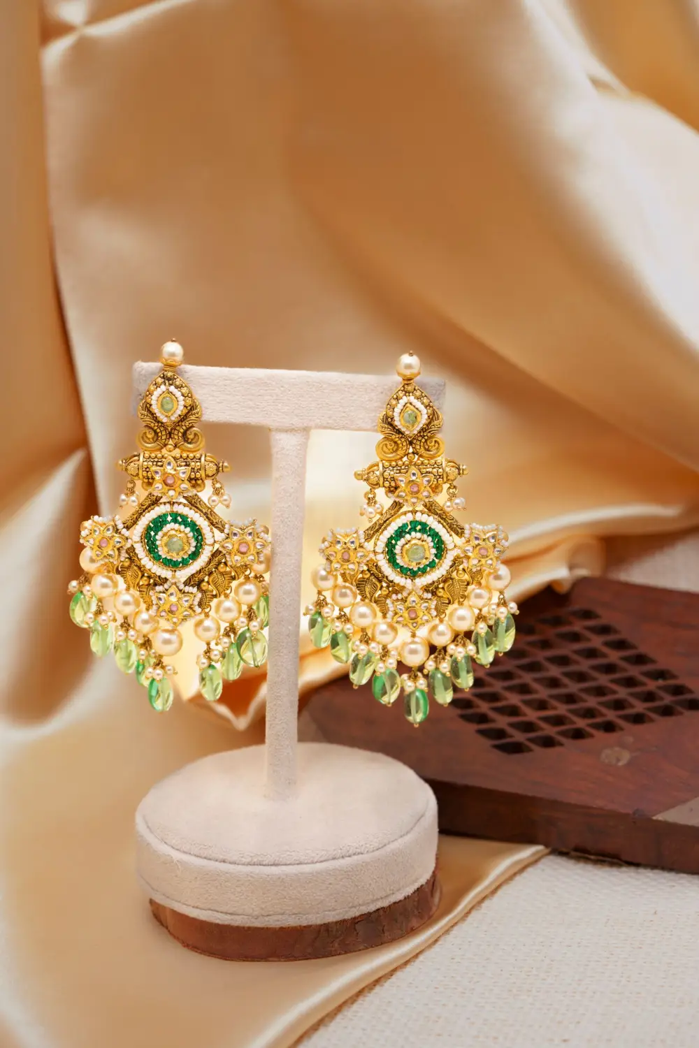 Gold chandelier earrings with green stones on a small stand