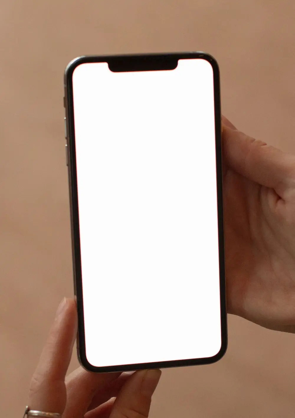 Two hands holding a phone against a warm plain wall